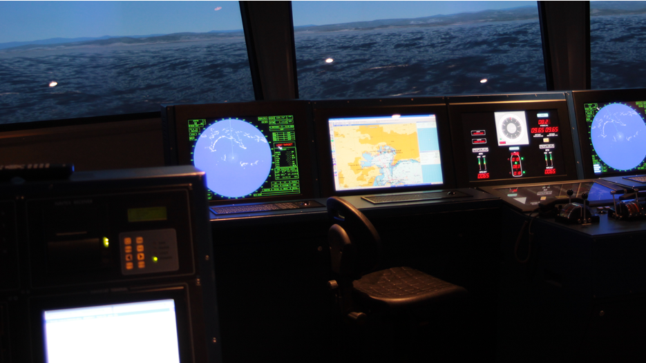 Laivo tiltelio simuliatoriaus valdymo konsolė su radarais, navigaciniais ekranais ir ECDIS sistema.